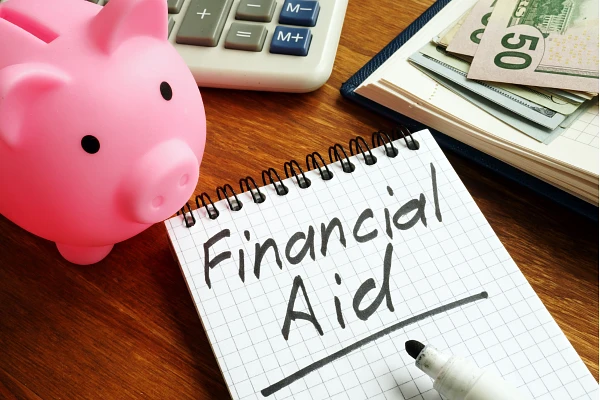 A piggy bank, a notebook with "Financial Aid" written on it, a calculator, and money are displayed on a wooden surface.