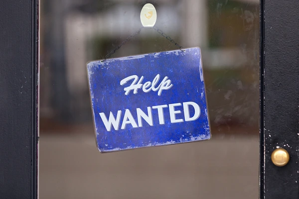 A blue "Help Wanted" sign hangs on a glass door.