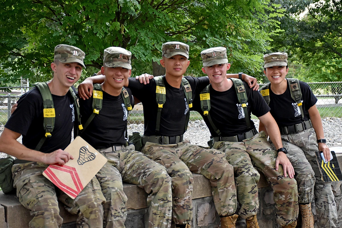 Five cadets in uniform smiling, sitting on a wall