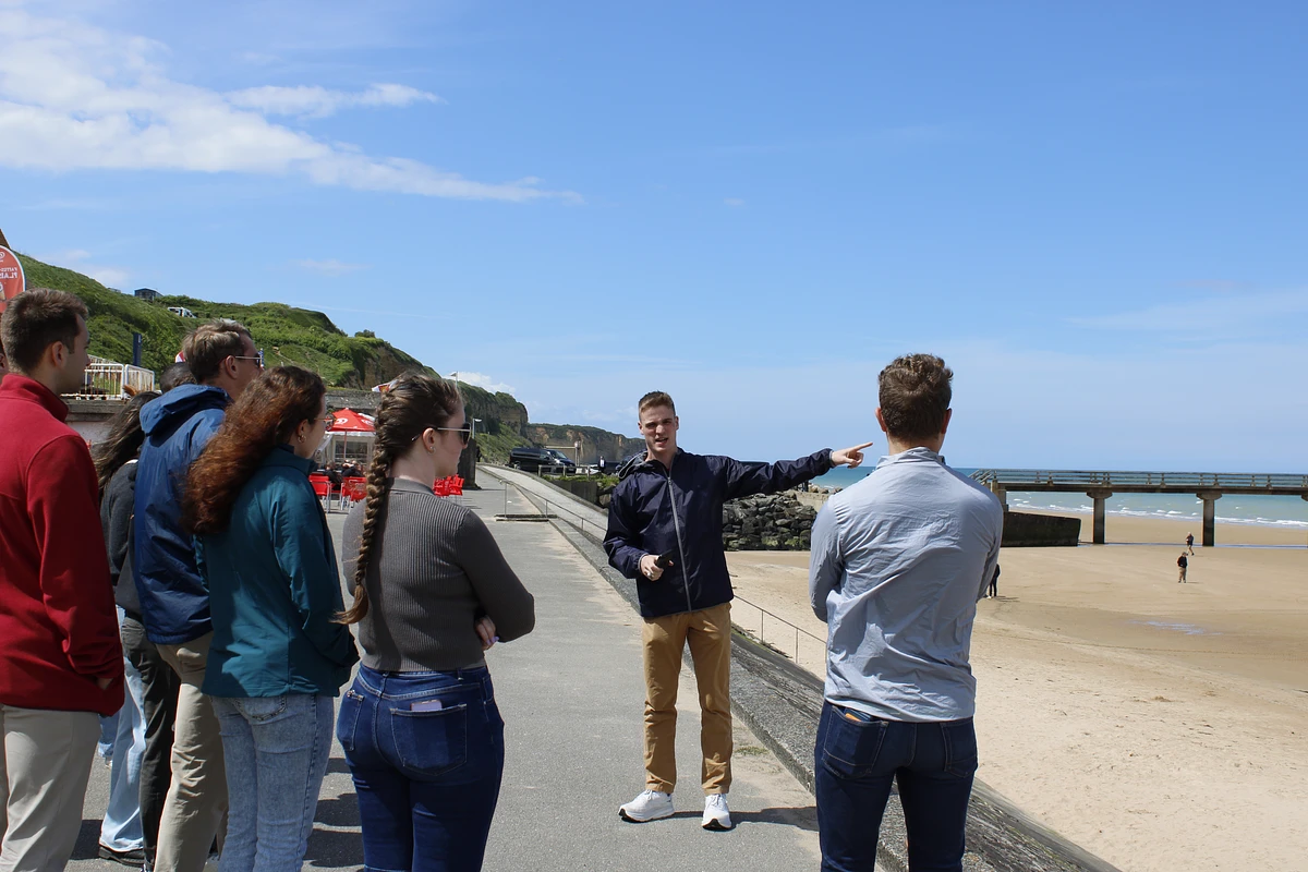 A cadet instructing a group of cadets points toward the surf while standing on Omaha Beach in Normandy, France.