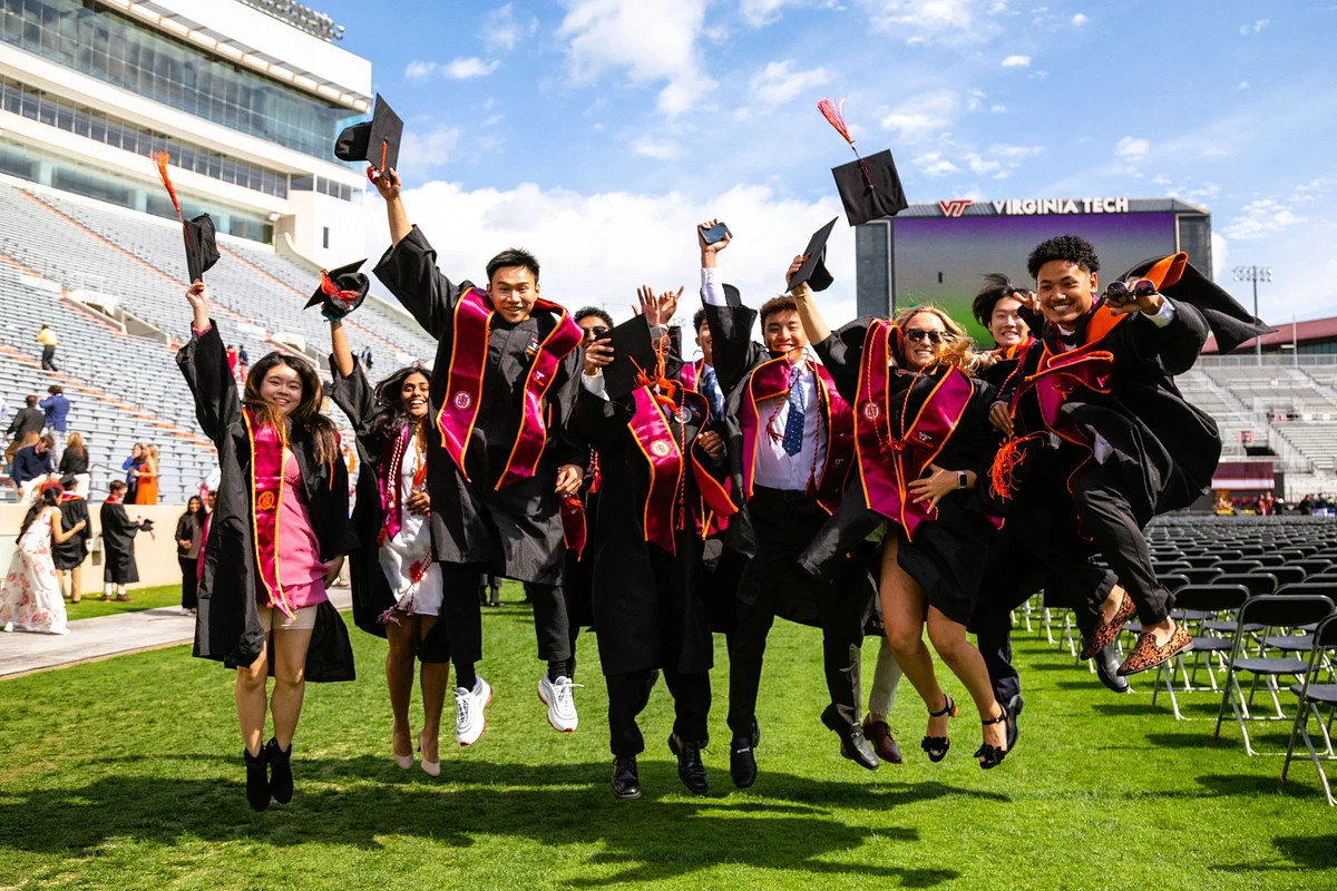 A group of graduates in caps and gowns joyfully jumps in celebration at the Virginia Tech commencement ceremony.
