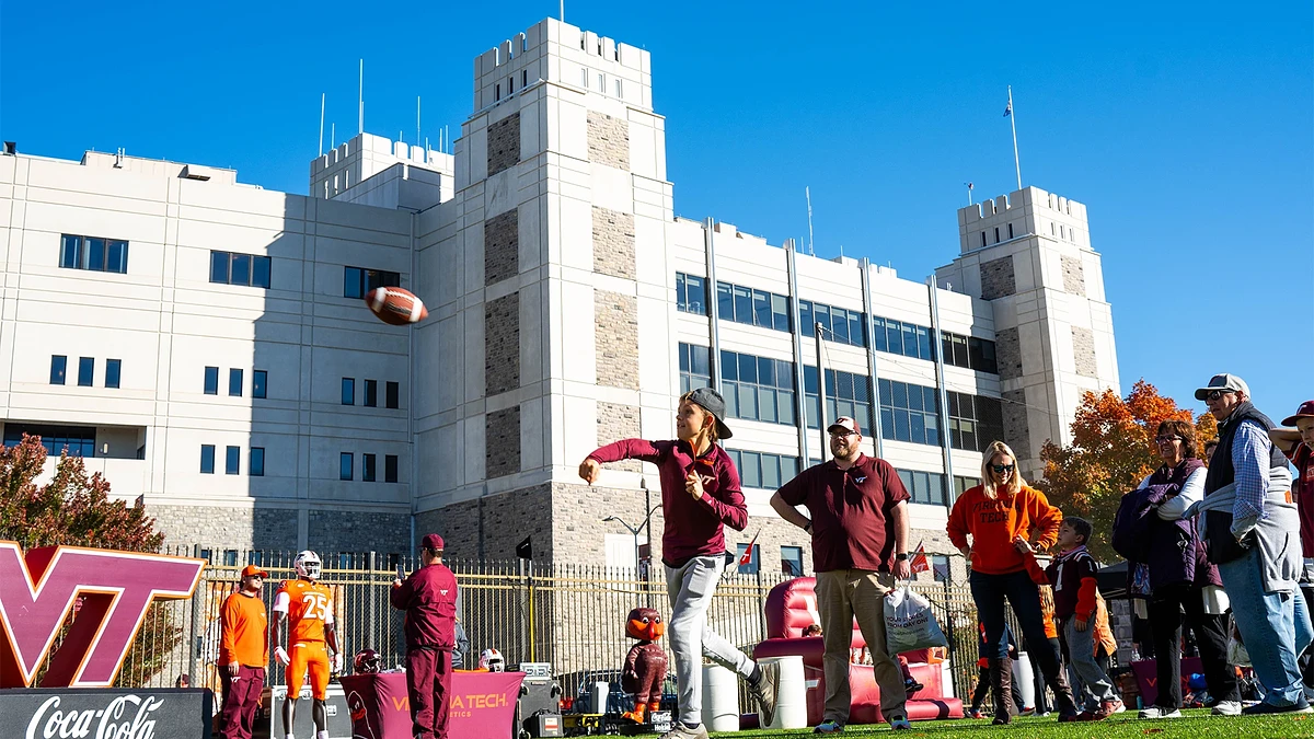 A person is playing football in front of a building with people gathered around on a clear day.