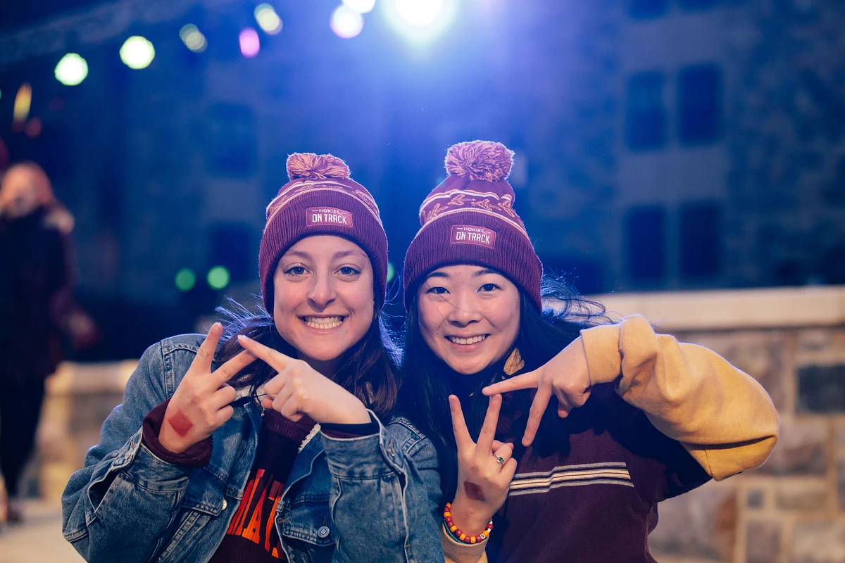 Two smiling people wearing matching "Hokies On Track" beanies pose together, making VT signs with their fingers.